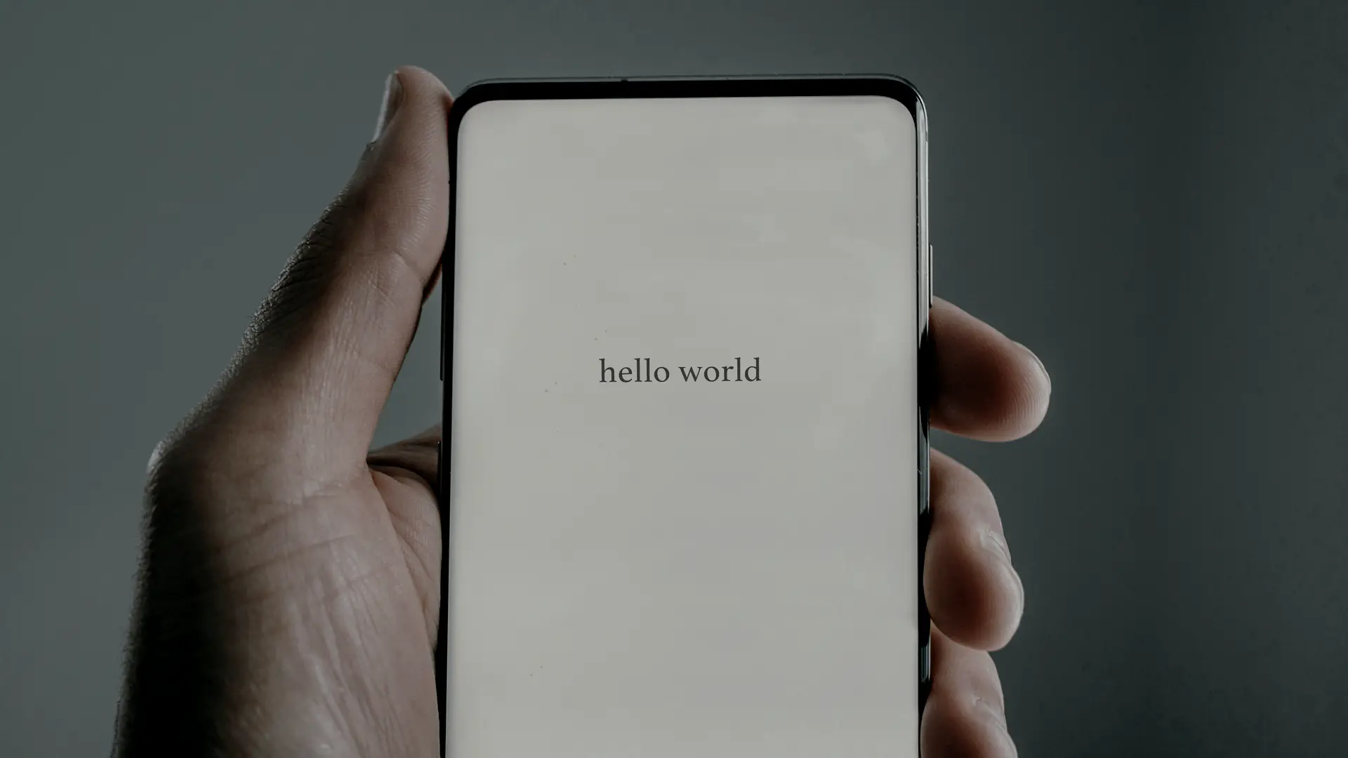 A hand holding a phone whose screen reads hello world
